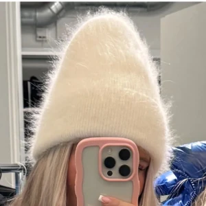 Vit stickad mössa - Superfin vit stickad mössa som är perfekt för kyliga dagar. Den är fluffig och ser riktigt mysig ut, med en ribbad kant som ger en snygg detalj. Passar perfekt till både vardag och vinteraktiviteter. Ett måste i garderoben för att hålla sig varm och stilren!