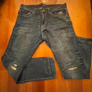 Polo Ralph Lauren Jeans - Ett par Polo Ralph Lauren slimfit jeans med snygga slitningar i storlek W33/L32. Byxorna är i mycket bra skick  (Se bild) och har bara används ett fåtal gånger. Byxorna är köpta på NK:)