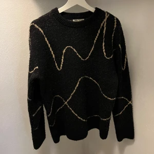 Svart stickad tröja från Zara - Säljer en svart stickad tröja från Zara med ett vågigt mönster i beige. Perfekt för höst och vinter, den är både stilren och bekväm. Storlek S/M. 