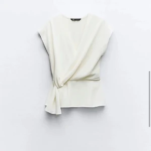 Vit omlottopp från Zara - Snygg vit omlottopp från Zara i ett mjukt och bekvämt material. Den är aldrig använd och tvättad en gång, toppen är i storlek small. Toppen har en elegant knytning i sidan och är ärmlös, vilket gör den perfekt för både vardag och fest. Passar bra till både jeans och kjol! Köpte den för 350 kronor och säljs nu för 280 kronor. Toppen säljs inte längre på Zara. Kan tänka mig att sänka priset! Skriv för fler bilder!