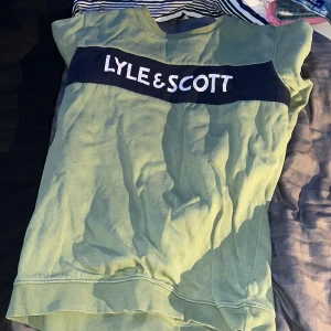 Grön tröja från Lyle & Scott - Säljer en grön tröja från Lyle & Scott i juniorstorlek 12/13 år. Tröjan har ett stort tryck med märkesnamnet över bröstet. Perfekt för vardagsbruk och passar bra till både jeans och shorts.