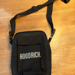 Svart axelväska från Hoodrich - Säljer en snygg svart axelväska från Hoodrich. Väskan har en justerbar rem och ett stort fack med dragkedja.
