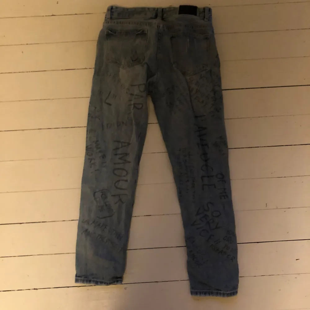 Säljer ett par unika blå jeans med coola textmönster över hela byxorna. . Jeans & Byxor.