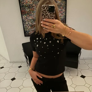 Svart topp med kristalldetaljer - Säljer en snygg svart topp från zara med små kristall liknande detaljer på framsidan. Toppen har korta ärmar och en normal passform. Den är knappt använd så i bra skick. 💞