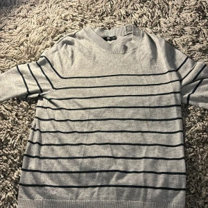 Grå randig tröja från 157 - Säljer en stilren grå tröja från 157 i storlek XS. Den har ett klassiskt randigt mönster i svart och är perfekt för både vardag och lite finare tillfällen. Tröjan är kortarämad och har en bekväm passform. Perfekt för höst och vår!