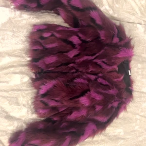 Lila och svart pälsjacka - Säljer en supercool lila och svart pälsjacka i syntetmaterial. Den är perfekt för att sticka ut på festen eller bara för att hålla sig varm och snygg under hösten. Jackan har en loose passform och långa ärmar. Den är i mycket bra skick och redo för nya äventyr!Priset kan diskuteras.