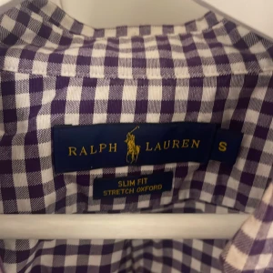 Rutig skjorta från Ralph Lauren - Säljer en snygg rutig skjorta från Ralph Lauren i storlek S. Skjortan är i slim fit och har en klassisk oxford-stil med stretch. Den är lila och vit med broderad logga på bröstet. Perfekt för både vardag och fest! 💜