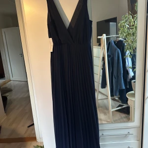 Mörkblå långklänning från AX Paris - Säljer en elegant mörkblå långklänning från AX Paris i nytt skick. Klänningen har en djup v-ringning och spetsdetaljer vid axelbanden. Perfekt för festliga tillfällen! 💙