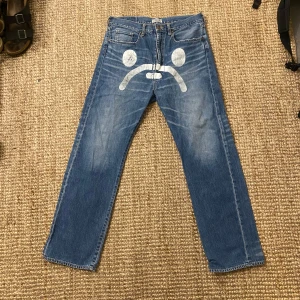 Vintage baby milo - Säljer ett par unika blå jeans från A Bathing Ape med coolt tryck fram och bak. De har en normal passform och är i bra skick. Perfekta för att sticka ut i mängden med sin kreativa design. Passar både till vardags och fest!