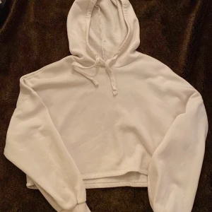 Vit croppad hoodie  - Mysig vit croppad hoodie från gina tricot storlek S. Perfekt för en avslappnad stil med sin mjuka fleece och bekväma passform. Den har en justerbar huva med dragsko och ribbade muddar vid ärmsluten. Perfekt för kyliga dagar eller mysiga hemmakvällar!
