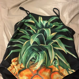 Baddräkt med ananasmönster - Säljer en supercool baddräkt från Mix med ett stort ananasmönster på framsidan. Den har smala axelband och är perfekt för sommarens badäventyr. Materialet känns mjukt och bekvämt mot huden. 