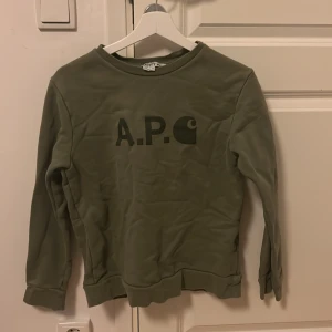 Grön  A.P.C. x Carhartt WIP Sweater - Säljer en snygg grön tröja från A.P.C. x Carhartt WIP i storlek S men passar xs. Tröjan har en enkel design med A.P.C.-logga på framsidan och är tillverkad i Portugal. Perfekt för en avslappnad stil!