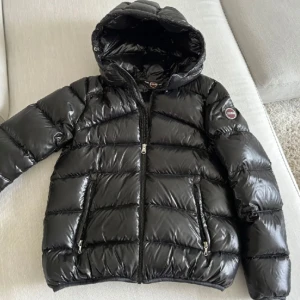 Svart pufferjacka från Colmar - Säljer en snygg svart pufferjacka från Colmar i mycket bra skick. Jackan har en glansig finish och är perfekt för kalla dagar. Den har en dragkedja framtill och två praktiska fickor med dragkedjor. Huvan är vadderad för extra värme. Perfekt för vintern! 🖤 stl 16y. Passar runt 155-170cm. Nypris är runt 5000kr
