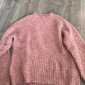 Rosa stickad tröja - Mysig rosa stickad tröja i ett härligt rutmönster. Perfekt för kyliga dagar med sin varma och bekväma passform. Tröjan har långa ärmar och ribbade kanter vid ärmslut och nederkant. Passar perfekt till både vardag och mysiga hemmakvällar.