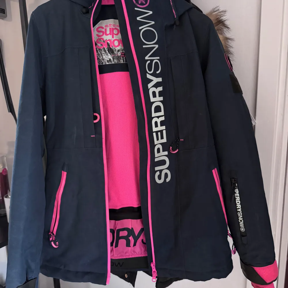 Säljer nu min gamla skidjacka från blå rosa Superdry Snow i storlek 36. Den har snöskydd, stora rymliga fickor och en ficka för liftkort på ärmen. Köpt på Zalando för 2 vintrar sen. Superdry Slalom Slice skidjacka för tjejer. Den här 2-i-1-jackan har ett snyggt och praktiskt ytterskal och en vadderad innerjacka för extra värme. Jackan är tillverkad av ett vattentåligt tekniskt material som andas. Ytterjackan har sex fickor varav en med hörlursöppning och glasögonduk, dubbla ärmslut med tumhål. . Jackor.