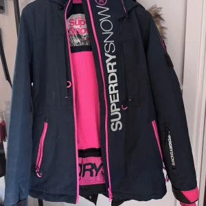 Superdry skidjacka - Säljer nu min gamla skidjacka från blå rosa Superdry Snow i storlek 36. Den har snöskydd, stora rymliga fickor och en ficka för liftkort på ärmen. Köpt på Zalando för 2 vintrar sen. Superdry Slalom Slice skidjacka för tjejer. Den här 2-i-1-jackan har ett snyggt och praktiskt ytterskal och en vadderad innerjacka för extra värme. Jackan är tillverkad av ett vattentåligt tekniskt material som andas. Ytterjackan har sex fickor varav en med hörlursöppning och glasögonduk, dubbla ärmslut med tumhål. 