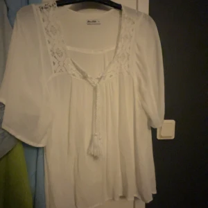 Vit blus från Miss Mila - Säljer en superfin vit blus från Miss Mila i storlek S. Blusen har vackra spetsdetaljer vid halsringningen och en söt knytning framtill. Den är perfekt för vår och sommar med sina trekvartsärmar och luftiga passform. Passar både till vardags och fest.