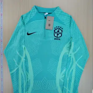 Säljer ett snyggt Brasilien träningsset från Nike. Tröjan är grön med lång ärm och har ett coolt mönster. Byxorna är mörkblå med gröna och blå detaljer. Perfekt för fotbollsträning eller som en sportig vardagsoutfit. Setet är i nytt skick och redo att användas!