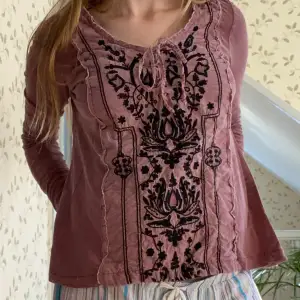 Säljer en superfin rosa/lila långärmad topp från Free People. Den har ett snyggt svart broderat mönster framtill och en knytning vid halsen. Toppen är i bra skick och passar perfekt till både vardag och fest.