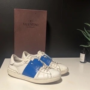 Valentino Garavani sneakers med blå detalj - Säljer ett par snygga Valentino Garavani sneakers i vitt skinn med en blå detalj över snörningen. Skorna är i använt skick och säljer dem pga att jag tröttnat på dem. Har haft dem nu drygt 1 år och rengjort dem ofta. Det tillkommer låda och certifikat att dem är äkta med två dustbags till skorna. Säljer dem till ett bra pris för vill bli av dem dem snabbt för att sedan köpa nya skor! Hör av er ifall ni har några frågor mvh Albin Landin 