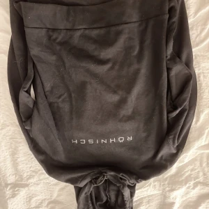 Svart hoodie från Rohnisch - Säljer en svart hoodie från Rohnisch i bra skick. Den är perfekt för både träning och vardag. Hoodien har en klassisk look med en stor ficka framtill och justerbar huva. Perfekt för höst och vinter! Hoddien är aldrig använd!