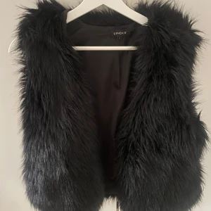 Svart pälsväst från Lindex - Säljer en superfin svart pälsväst från Lindex i storlek S. Perfekt för att ge din outfit en lyxig touch. Västen är i  bra skick och passar perfekt för höst och vinter. Den är mjuk och bekväm att bära, och ger en stilren look.