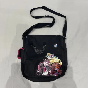 Svart axelväska med Monster High tema💕🧛‍♀️ - justerbar axelrem och en kedjedetalj! Perfekt för skolan då den rymmer dator eller iPad osv. Den är rymlig och har flera fack inuti för enkel organisering. Baksidan är helt plain så tog ingen bild. Superbra skick inga defekter