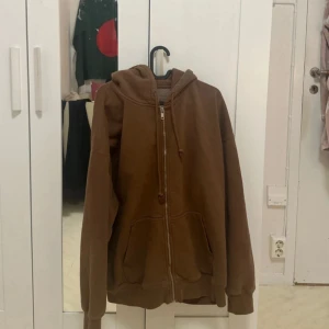 Brun hoodie från Brandy Melville - Mysig brun hoodie från Brandy Melville i bra skick. Perfekt för höst och vinter med dragkedja och fickor framtill. Den har en avslappnad passform och är superbekväm för vardagsbruk. Ett måste i garderoben för kyliga dagar!