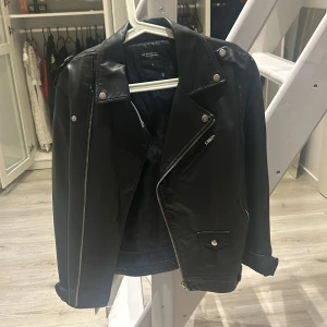Svart skinnjacka från Biker - Säljer en snygg svart skinnjacka från Biker i mycket bra skick. Den har en cool asymmetrisk dragkedja och stiliga knappar. Perfekt för höst och vår, och funkar lika bra till fest som till vardags. Jackan har långa ärmar och en klassisk bikerstil. Passar perfekt för dig som vill ha en edgy look! 🖤