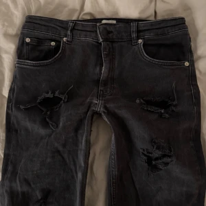 Svarta jeans med slitningar - Säljer ett par svarta jeans med coola slitningar på framsidan. De har en klassisk femficksdesign och är i bra skick trots slitningarna som ger dem en edgy look. Perfekta för en avslappnad stil eller en utekväll. 