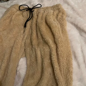 Beige mjukisbyxor med snörning - Supermysiga beige mjukisbyxor i fleece med svart snörning i midjan. Perfekta för att hålla sig varm och bekväm hemma. Byxorna har en loose passform som ger en avslappnad känsla.
