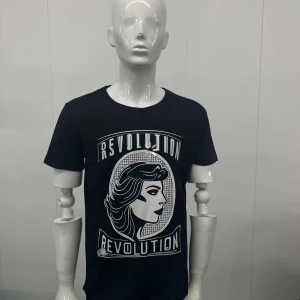 Svart t-shirt med tryck - Snygg svart t-shirt med ett coolt tryck av en kvinna och texten 'Revolution'. Perfekt för en avslappnad stil med en touch av attityd. Rund hals och korta ärmar gör den bekväm och lätt att bära.