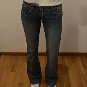 Blå jeans från Diwa - Snygga blå jeans från Diwa med unika broderade detaljer på bakfickorna. De har en lågmidjad passform och en klassisk bootcut-stil. Stenarna på bakfickorna har tyvärr ramlat av, men förövrigt inget slitage ⭐️🙌🏼