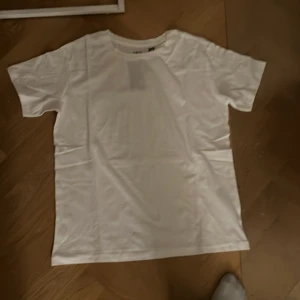 Vit t-shirt - En klassisk vit t-shirt med rund hals och korta ärmar. Perfekt basplagg för alla tillfällen. Tillverkad i mjukt material för extra komfort.