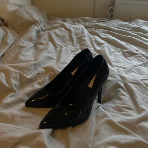 Svarta pumps med spetsig tå - Snygga svarta pumps i lackmaterial med hög klack och spetsig tå. Klassisk design och funkar perfekt till likaså klänning till byxor. Dem är köpta second hand men jag själv har aldrig använt dom och ser oanvända ut!