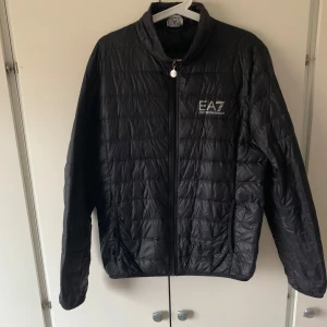 Svart  jacka från EA7 - Snygg svart quiltad jacka från EA7 med dragkedja framtill. Perfekt för kyligare dagar med sin stilrena design och bekväma passform. Jackan har långa ärmar och en diskret logga på bröstet.