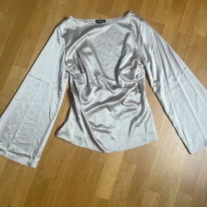 Beige satinblus från Boohoo - Elegant beige blus i satin från Boohoo med långa vida ärmar och rynkad midja. Helt ny aldrig använd.