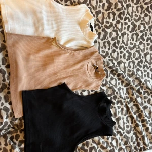 Ribbade croppade linnen i tre färger - Säljer tre snygga ribbade linnen i svart, beige och vit. Dessa ärmlösa toppar har en hög hals och är croppade. Använd endast den svarta en gång.