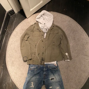 Unik Fieldjacket - Säljer en olivgrön jacka med unikt tryck på baksidan. Jackan har långa ärmar och knappar framtill. Perfekt för lager på lager och avslappnad stil. Till riktigt bra pris men förhandlingsbart. Mvh.