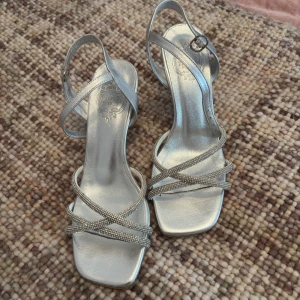 Silvriga sandaler med klack - Eleganta silvriga sandaler med klack och smala remmar som korsar över foten. Storlek 37 från NOVITA💕