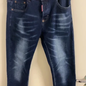 Mörkblå jeans slitningar - Snygga mörkblå jeans med coola slitningar och en klassisk femficksdesign. Perfekta för en avslappnad stil med en touch av edge. De har en knappgylf och är tillverkade i ett bekvämt denimtyg.