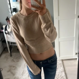 Beige stickad tröja - Säljer en beige stickad tröja med långa ärmar och ribbade kanter. Tröjan är croppad och passar perfekt för en stilren look. Perfekt för kyligare dagar. Helt ny har aldrig använt❤️original pris 129