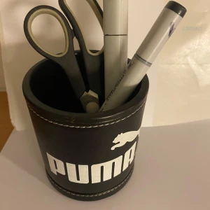 Svart pennställ från Puma - Snyggt svart pennställ från Puma med vit logga. Perfekt för att hålla ordning på pennor och saxar på skrivbordet. Tillverkad i ett robust material med stilren design. Aldrig använt så fint skick 