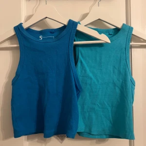 Två ribbade linnetoppar i blå nyanser - Säljer två snygga ribbade linnetoppar i olika blå nyanser. Perfekta för sommardagar. De är ärmlösa och har en stilren design som passar till det mesta. Perfekt för dig som vill ha något enkelt men stilrent i garderoben. Mörkblå enbart använd en gång, turkos aldrig använd! Kan säljas styckvis för 40kr/styck