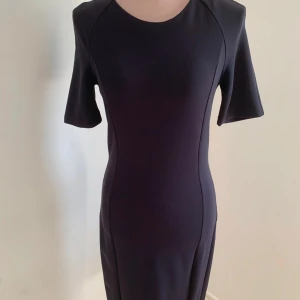 Svart klänning med trekvartsärm - Elegant svart klänning med trekvartsärm och figurnära passform. Perfekt för en stilren look. Klänningen har en enkel design som framhäver silhuetten.