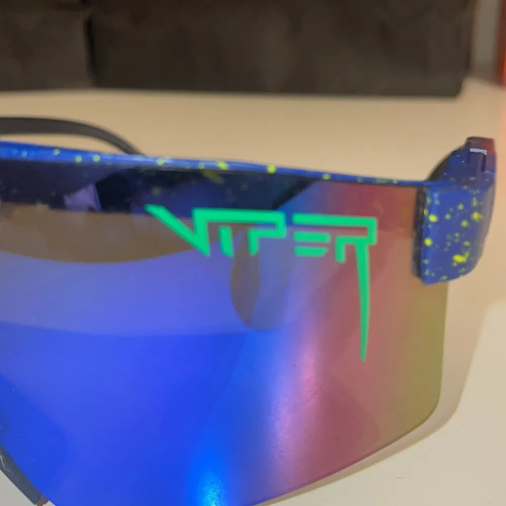 Snygga blå solglasögon från Pit Viper med spegelglas i grönt och blått. Bågarna har ett coolt stänkmönster i gult och justerbara skalmar för perfekt passform. Perfekta för en sportig look!. Asusteet.