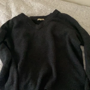 Svart stickad tröja - Säljer en svart stickad tröja med v-ringning. Tröjan har långa ärmar och är perfekt för kyligare dagar. Enkel och stilren design som passar till det mesta.
