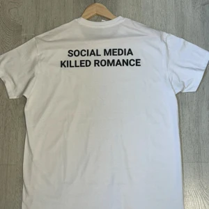 Vit t-shirt med text - Säljer en vit t-shirt med texten 'SOCIAL MEDIA KILLED ROMANCE' tryckt i svart på baksidan. T-shirten har en klassisk passform och är kortärmad. Perfekt för en avslappnad stil med ett statement.