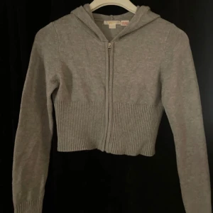 Grå croppad hoodie från Gina Tricot - Säljer en stilren grå croppad hoodie från Gina Tricot. Den har en dragkedja framtill och en mysig huva. Perfekt för en avslappnad look. Passar bra till jeans eller leggings. 🩶