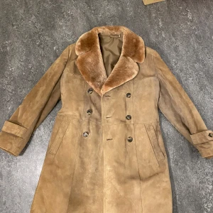 Beige mockakappa med pälsdetaljer - Säljer en elegant beige mockakappa med mjuk pälsdetalj på kragen. Kappan har en dubbelknäppt design med knappar och långa ärmar. Perfekt för kyligare dagar med sin stilrena look och bekväma passform. Helt ny bara testad!